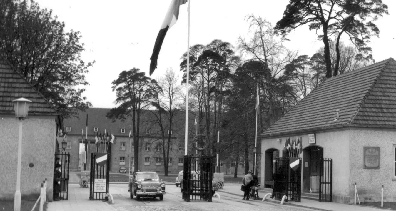 Eingangstor mit gehisster französischer Flagge, einem Auto und ein paar Menschen